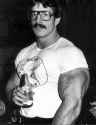 Mike-Mentzer-with-huge-arm-drinking-Perrier