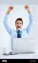 business-victory-portrait-of-a-businessman-sitting-at-his-desk-with-his-computer-in-front-of-him-and-cheering-with-his-arms-raised-above-his-head-2M03Y2T