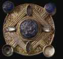 Gilt-copper alloy circular mount set with glass. Circular disc with four projecting settings for dark blue glass studs with recessed stepped pattern on surface (two now missing).-8thC-9thC