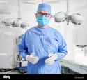 portrait-of-doctor-in-glasses-looking-at-camera-while-standing-in-operating-room-man-surgeon-in-sterile-gloves-blue-surgical-uniform-and-protective-face-mask-ready-for-plastic-surgery-in-clinic-2E1PDMR