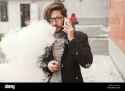 young-hipster-man-with-a-beard-and-glasses-smokes-an-electronic-cigarette-HPGW7K