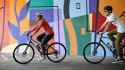 two-riders-on-trek-hybrid-bicycles-in-front-of-painted-mural-wall