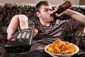 man with remote watching tv and drinking beer and eating chips