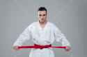 graphicstock-picture-of-sportsman-dressed-in-kimono-practice-in-karate-while-tightening-red-belt-isolated-over-grey-background-look-at-camera_BuwSNsU2g_SB_PM